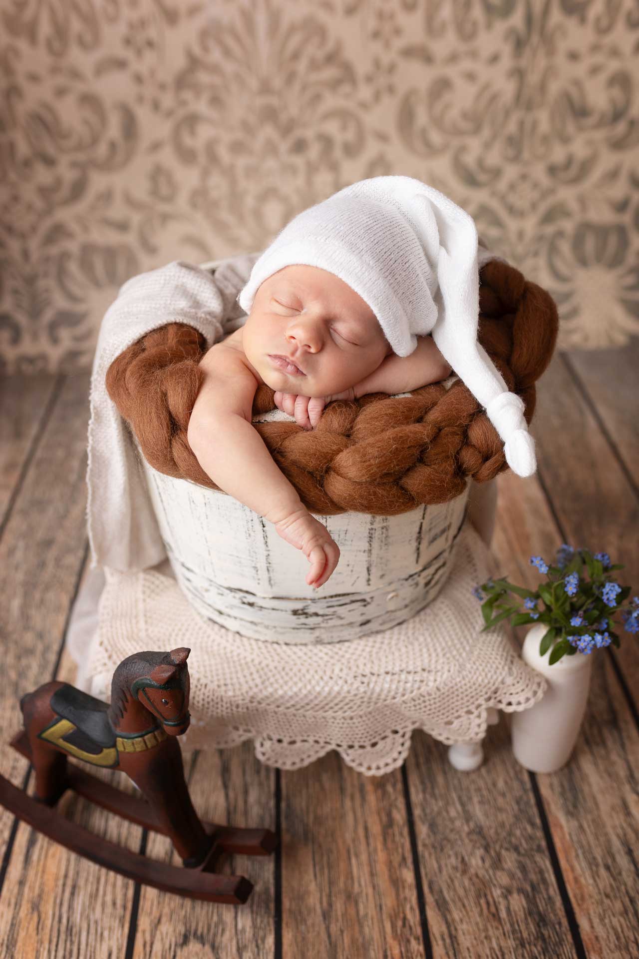 Ein Baby mit langer, weißer Zipfelmütze in einem Korb beim Babyshooting | Angebot Fotoshootings